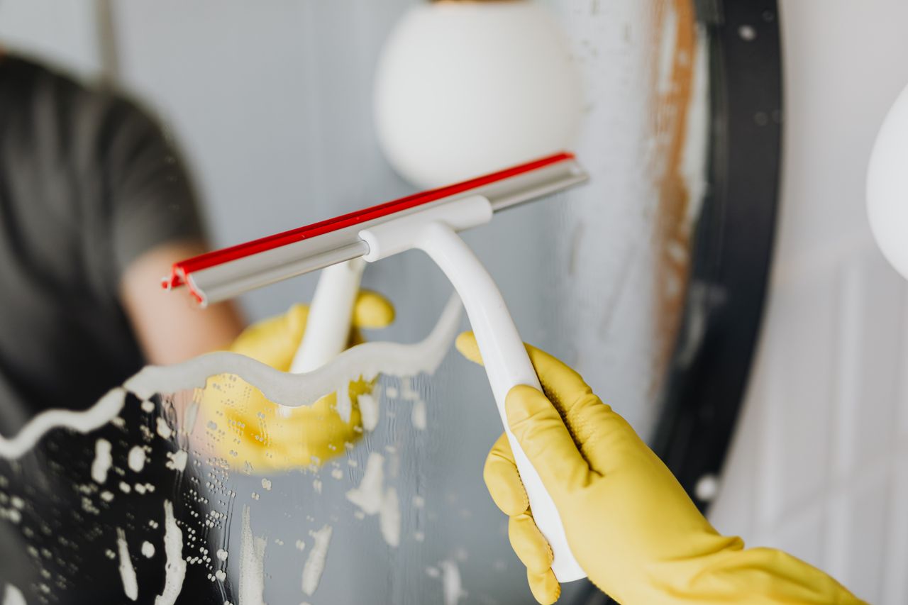 team-01 Faceless person in yellow rubber gloves using scraper to remove soapy water from mirror in bathroom