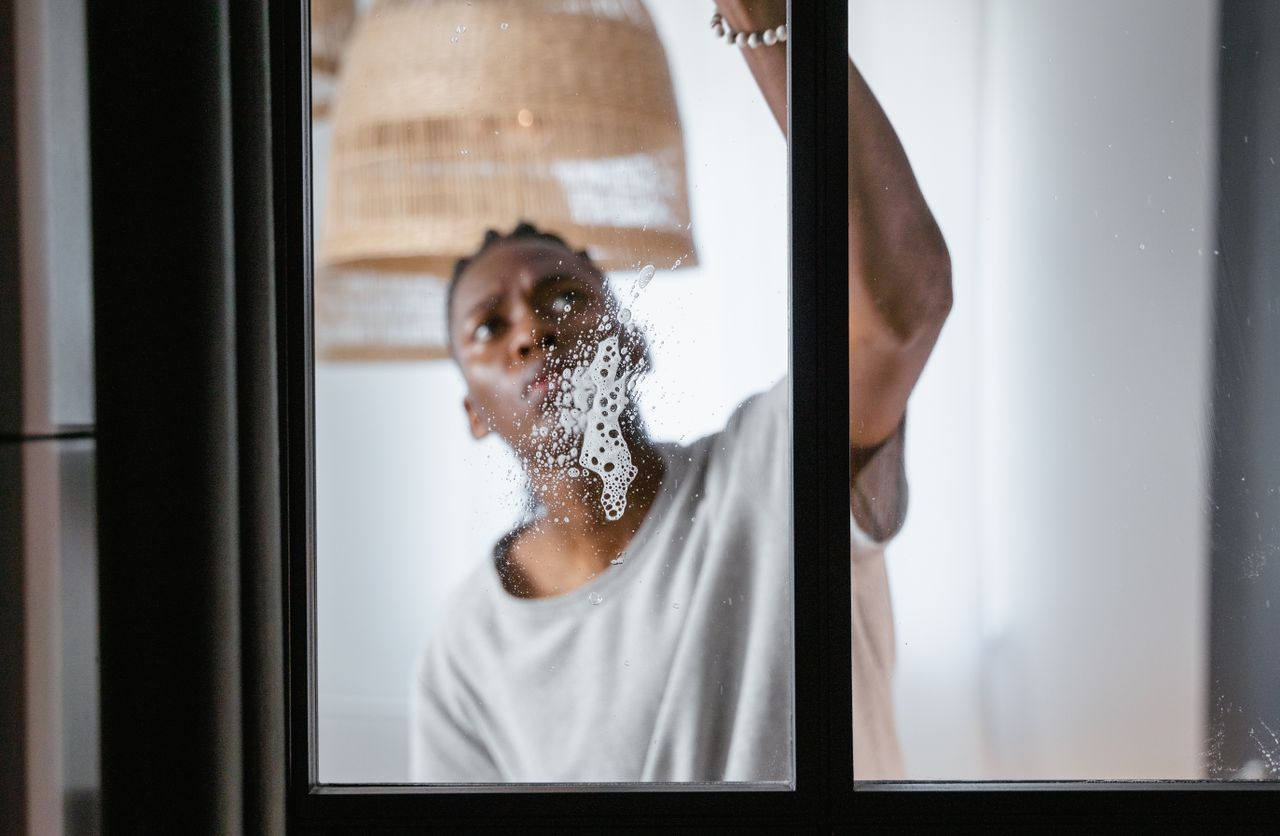 team-04 An adult male cleaning a glass window indoors, focusing on household chores and cleanliness.