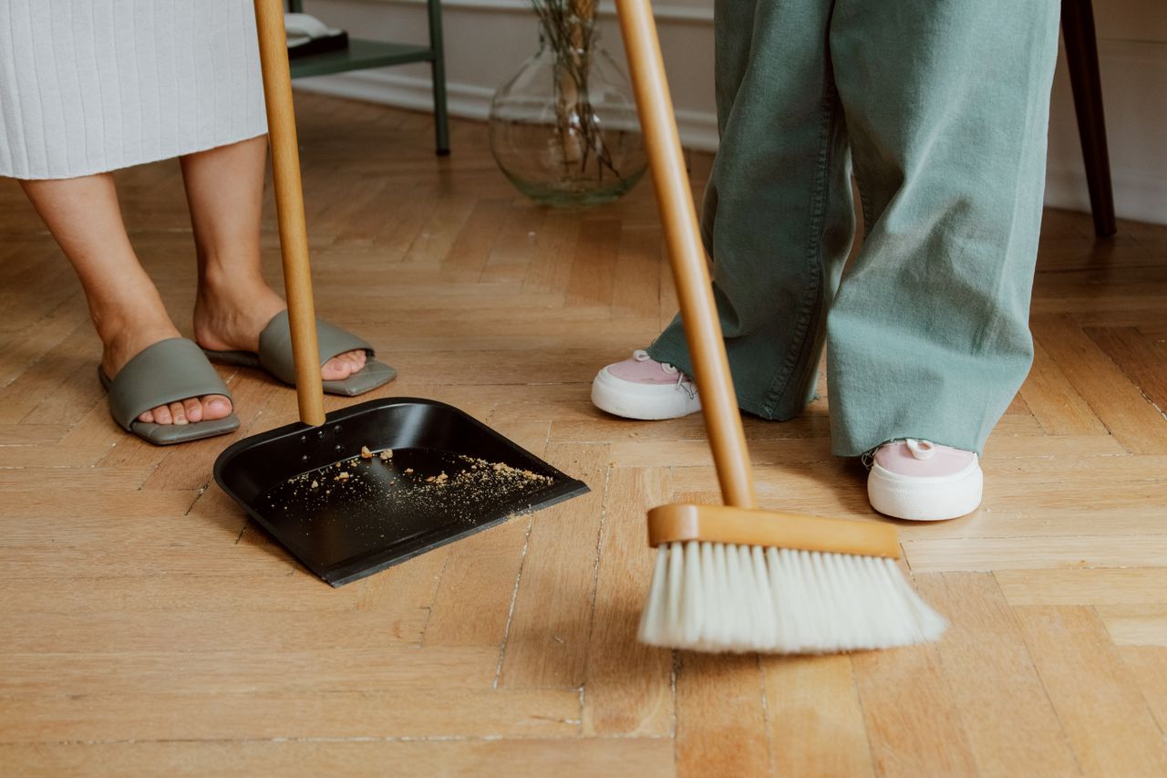 journey Close-up of people cleaning wooden floor with broom and dustpan indoors.
