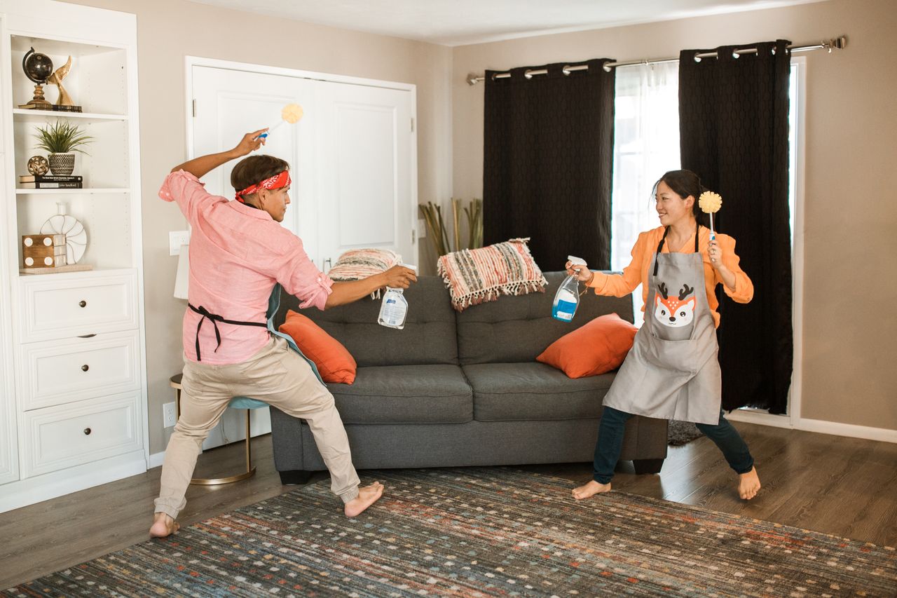 services-04 A joyful couple engages in a playful cleaning fight in their living room, showcasing light-hearted domestic life.